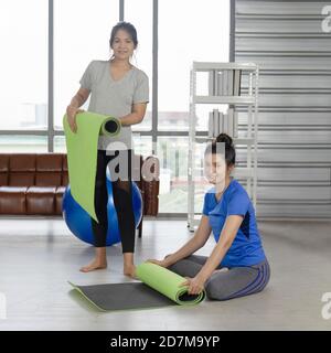 Zwei asiatische Frauen mittleren Alters Rollen eine Gummimatte für Yoga nach Beendigung des Trainings drinnen. Stockfoto