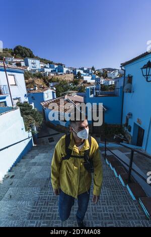 Vertikale Aufnahme eines Mannes mit einer gelben Jacke und Eine Gesichtsmask, während man die Treppe im Freien hochklettert Stockfoto