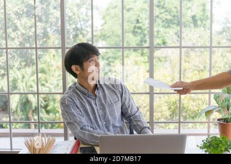 Eine Hand, die einem trauernden asiatischen Mann Dokumente mit schlechten Nachrichten liefert: Ein verzweifelter Unternehmer wird entlassen, versteckt sich weinend, enttäuscht vom Bankrott Stockfoto