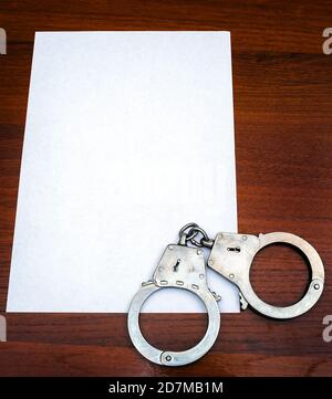 Handschellen und leeres Papier auf dem Holztisch Nahaufnahme Stockfoto