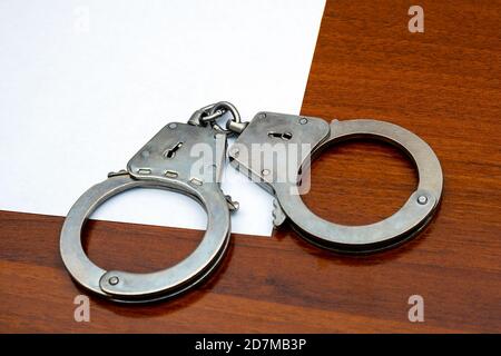 Handschellen und leeres Papier auf dem Holztisch Nahaufnahme Stockfoto