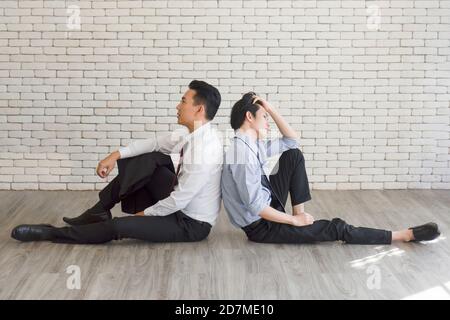 Zwei männliche Angestellte saßen auf dem Boden und zeigten Anzeichen von Stress durch Überlastung. Stockfoto