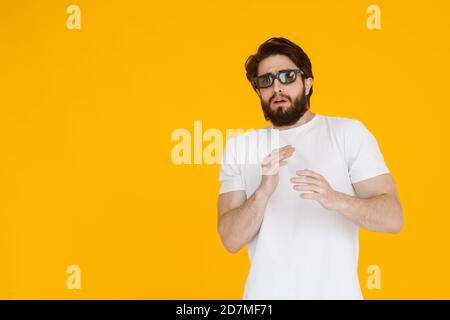 Porträt eines zotteligen, bärtigen, verängstigten Mannes in 3D-Brille mit offenem Mund und großen Augen, auf gelbem Hintergrund. Stockfoto