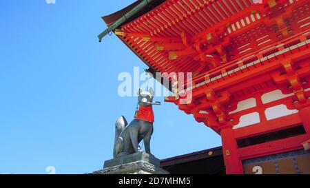 Japanischer schintoistischer Schrein Tempel Hund Statue hält Schlüssel in seinem Mund mit rotem Schal Gold Details blauen Himmel Luxus reisen Rotes Gebäude in kyoto japan Stockfoto