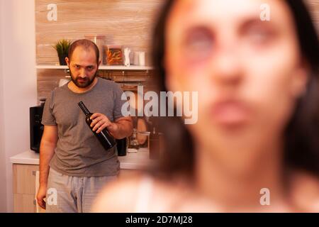 Missbräuchlicher Ehemann, der Alkohol trinkt und seine traumatisierte Frau wegen seiner häuslichen Gewalt ansieht. Aggressiver Ehemann missbraucht Verletzungen erschrocken hilflos, verletzlich, ängstlich, geschlagen und in Panik versetzt Frau. Stockfoto