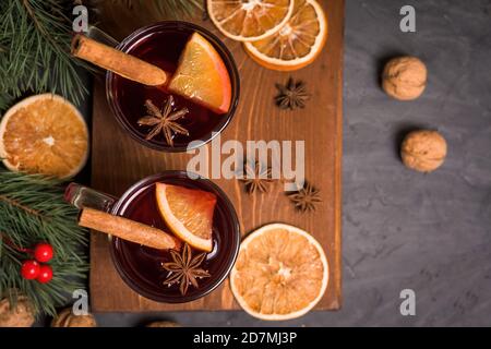 Roter würziger WeihnachtsGlühwein auf Rotweinbasis mit orangen und würzigen Zimtstangen, Sternanis, auf schwarzem Hintergrund. Rezept für saisonale Getränke Stockfoto