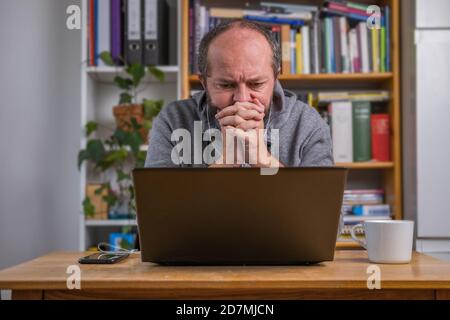 Mann, der online vom Heimbüro auf Computer-Laptop hinter vintage Schreibtisch arbeitet, konzentriert, mit Kopfhörern, Höre Online-Meeting Stockfoto