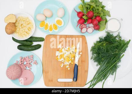 Schritt für Schritt Rezept für russische kalte Okroshka-Suppe, Zutaten für hausgemachte Okroshka geschnitten mit einem Messer-Wurst, Kräuter, Eier, Gurken, Kartoffeln, Radi Stockfoto