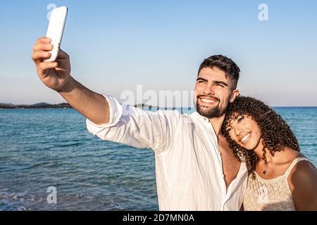 Junge Mischrennsportler Paar bei Sonnenuntergang im Stehen Die Küste macht ein Selbstporträt mit dem Smartphone - Kaukasischer Mann mit Spaß Schießen ph Stockfoto
