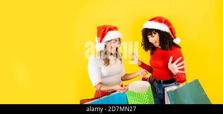 Nette kaukasische blonde junge Frau öffnen ihre Einkaufstasche zeigt An ihre schwarze hispanische Freundin - zwei tausendjährige multirassische Shopper-Frauen mit S Stockfoto