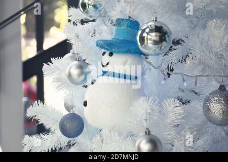 Ein blaues Schneemann-Spielzeug und viele silberne Bälle hängen Auf weißem Christbaum für dekorierte das Wohnzimmer Stockfoto