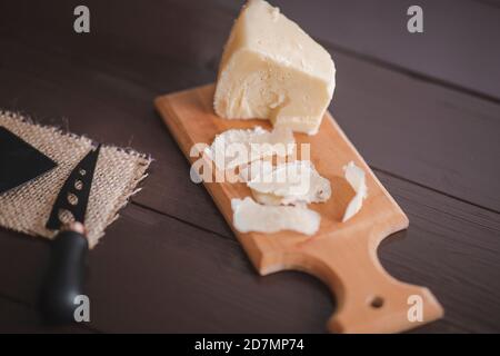 Komponierte Nahaufnahme Detailansicht von gealtertem Cheddar-Käse mit Käsemesser-Set, über vintage brauner Holzkulisse Stockfoto