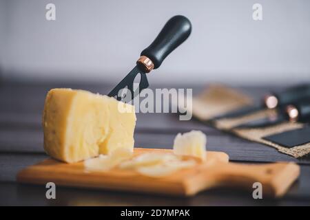 Komponierte Nahaufnahme Detailansicht von gealtertem Cheddar-Käse mit Käsemesser-Set, über vintage brauner Holzkulisse Stockfoto