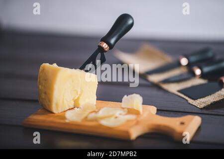 Komponierte Nahaufnahme Detailansicht von gealtertem Cheddar-Käse mit Käsemesser-Set, über vintage brauner Holzkulisse Stockfoto