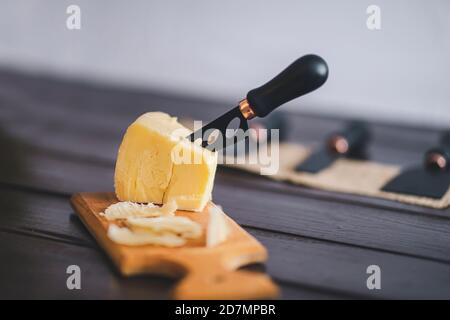 Komponierte Nahaufnahme Detailansicht von gealtertem Cheddar-Käse mit Käsemesser-Set, über vintage brauner Holzkulisse Stockfoto