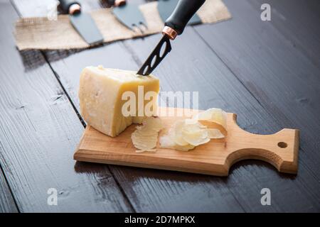 Komponierte Nahaufnahme Detailansicht von gealtertem Cheddar-Käse mit Käsemesser-Set, über vintage brauner Holzkulisse Stockfoto