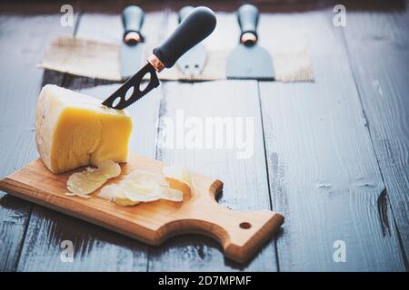 Komponierte Nahaufnahme Detailansicht von gealtertem Cheddar-Käse mit Käsemesser-Set, über vintage brauner Holzkulisse Stockfoto