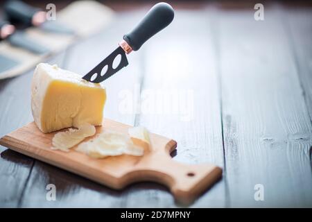 Komponierte Nahaufnahme Detailansicht von gealtertem Cheddar-Käse mit Käsemesser-Set, über vintage brauner Holzkulisse Stockfoto