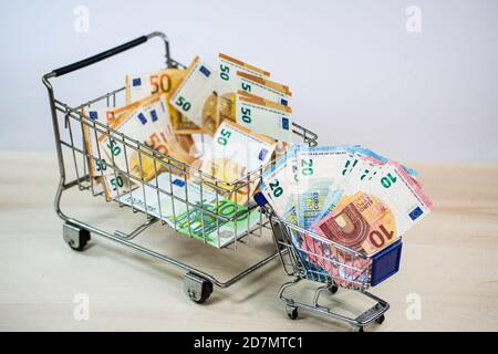 Kleiner und großer Einkaufswagen voller Geld, symbolisch Stockfoto