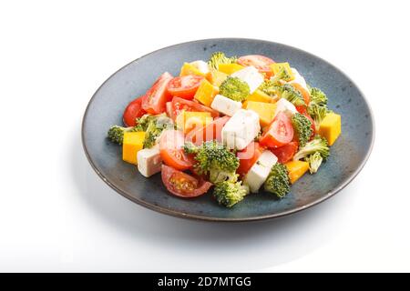 Vegetarischer Salat mit Brokkoli, Tomaten, Feta-Käse und Kürbis auf einer blauen Keramikplatte isoliert auf weißem Hintergrund, Seitenansicht, Nahaufnahme, Stockfoto