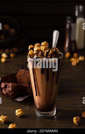 Hohe Glas Tasse mit Schokolade Milchshake und Karamell Popcorn und Schokoladenmuffin auf Holzhintergrund Stockfoto