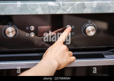 Weibliche Hand drehen auf den Ofen, um einen Kuchen zu Hause zu machen. Nahaufnahme des Backofenschalters. Ansicht des schwarzen Elektroofens, Drehknopf mit Heißluftsymbol. Die Konz Stockfoto