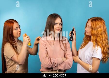 Aromaprüfung. Zwei Beratermädchen testen neue Düfte an einem dritten Mädchen. Produkttester für Frisuren. Foto auf blauem Hintergrund Stockfoto