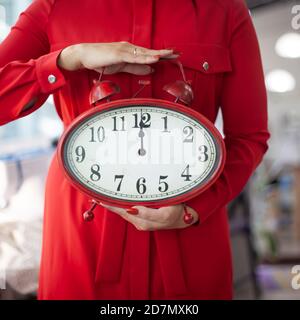 Frau in rotem Kleid hält mit Händen eine riesige Uhr Zeigt 12 Mitternacht von Silvester Stockfoto