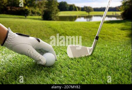 Golfplatz, Golfball und Club auf grünem Golfplatz Rasen, blau bewölkt Himmel Hintergrund. Golfer Hand in Handschuh hält einen Ball, Nahaufnahme. Stockfoto