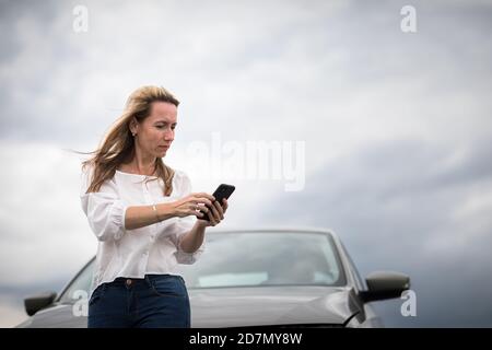 Ziemlich Frau mittleren Alters, die Autoprobleme hat - zusammengebrochenes Auto auf der Seite der Straße, die Versicherungsgesellschaft um Hilfe zu rufen Stockfoto