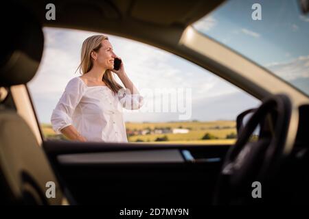 Hübsche Frau im mittleren Alter am Steuer ihres Autos, eine Pause auf einer langen Reise, einen Anruf zu machen Stockfoto