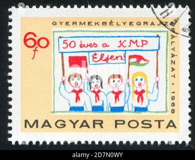 UNGARN - UM 1968: Stempel gedruckt von Ungarn, zeigt vier Pioniere mit Transparent zur Begrüßung der Kommunistischen Partei, um 1968 Stockfoto