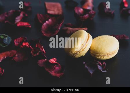 Nahaufnahme des Frühstücks am Morgen mit gelben Makronen Zitronengeschmack. Nahaufnahme von französisch Dessert auf dem schwarzen Hintergrund und Blumen um in einem einfachen Vin Stockfoto