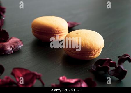 Nahaufnahme des Frühstücks am Morgen mit gelben Makronen Zitronengeschmack. Nahaufnahme von französisch Dessert auf dem schwarzen Hintergrund und Blumen um in einem einfachen Vin Stockfoto