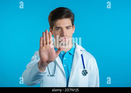 Porträt eines seriösen Arztes in professionellen medizinischen weißen Mantel zeigt Ablehnung Geste von Anschlag Handfläche Zeichen. DOC man isoliert auf blauem Hintergrund. Stockfoto