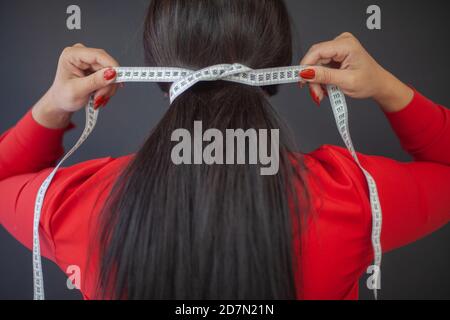 Weibliche Modedesignerin in rotem Kleid wickelte ihr Haar mit Maßband Stockfoto