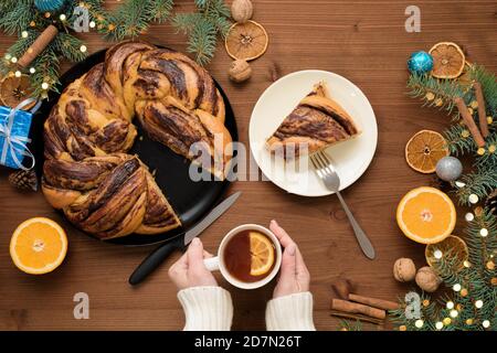 Schokoladen-Weihnachtsgroßmutter in Form eines Kranzes mit Orangensirup auf einem in Stücke geschnittenen Teller. Weihnachtsschmuck auf einem Holztisch. Stockfoto