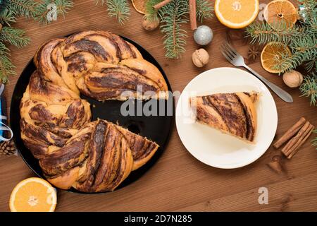 Schokoladen-Weihnachtsgroßmutter in Form eines Kranzes mit Orangensirup auf einem in Stücke geschnittenen Teller. Weihnachtsschmuck auf einem Holztisch. Stockfoto