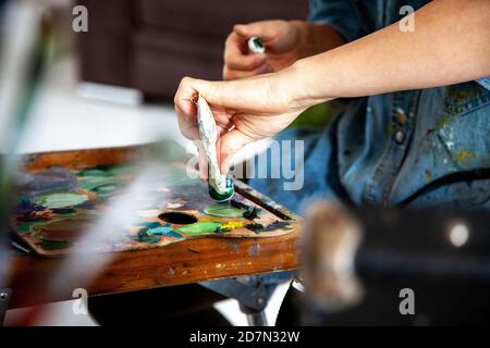 Künstlerin Hand drückt eine Tube mit gelb orange Öl Malen auf Holzpalette im Kunststudio Stockfoto