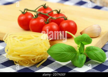 Pasta-Zutaten: Ungekochte Tagliatelle, Kirschtomaten auf Stiel und frische Basilikumblätter Stockfoto