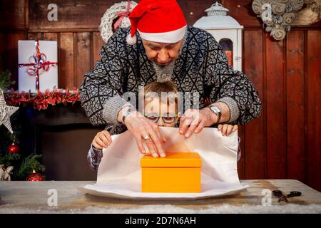 Glücklicher Großvater lehrt seinem Enkel, wie man Weihnachten einwickelt Geschenke auf dem Tisch Stockfoto