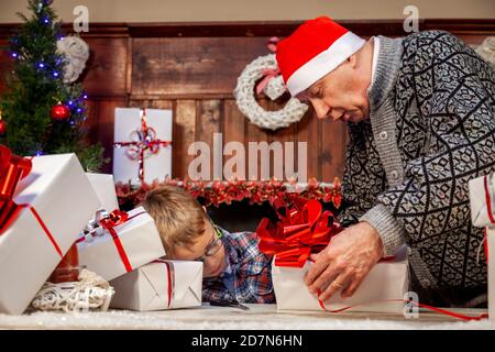 Glücklicher Großvater lehrt seinem Enkel, wie man Weihnachten einwickelt Geschenke auf dem Tisch Stockfoto