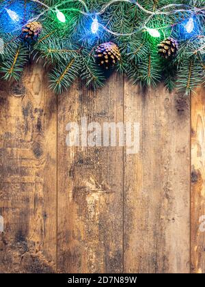Grüne Tannenzweige und Weihnachtslichter auf dunklem Holztischhintergrund. Kreatives Layout Rahmen aus Tannenzweigen Tannenzapfen auf Holzbac Stockfoto
