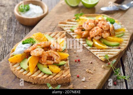 Knuspriger großer Toast mit gegrillten Garnelen auf Avocado und Orange Scheiben mit Dill Limette Sauce Stockfoto