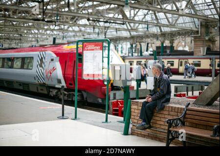 Glasgow Central Station Juli 2010. Ein Mann sitzt an einer Wand, nachdem Passagiere den Zug bestiegen haben, und scheint zu denken oder nachzudenken. Virgin Trains. Straße. Stockfoto