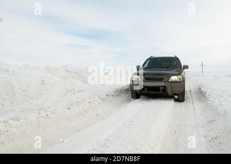 Männlicher Fahrer in einem schwarzen schmutzigen Auto auf einer vom Schnee gerodeten Winterstraße, driftet entlang der Straße Stockfoto