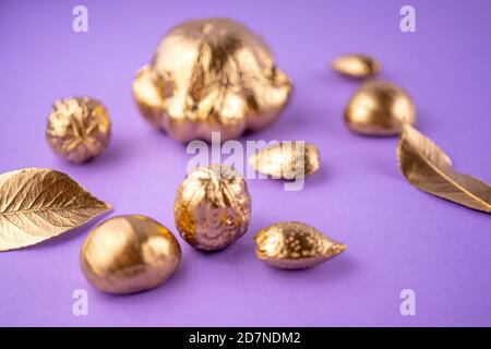 Verschwommenes Fokusfoto. Kürbisse, Nüsse und Blätter in Gold auf violettem Hintergrund gemalt. Flaches Layout mit Platz für Text. Stockfoto