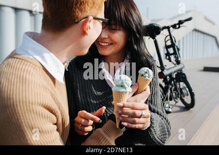 Unbeschwertes Paar, das draußen mit Eis sitzt, lächelt, mit Stirn berührt Stockfoto