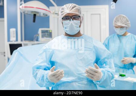 Moderner Chirurg mit gemischter Rasse in Schutzmaske, Handschuhen und Brillen Stockfoto