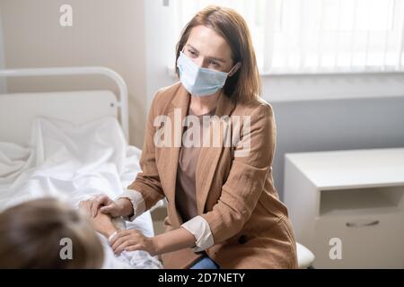 Junge Frau in Casualwear und Schutzmaske Unterstützung kranken Freund Mit covid Stockfoto